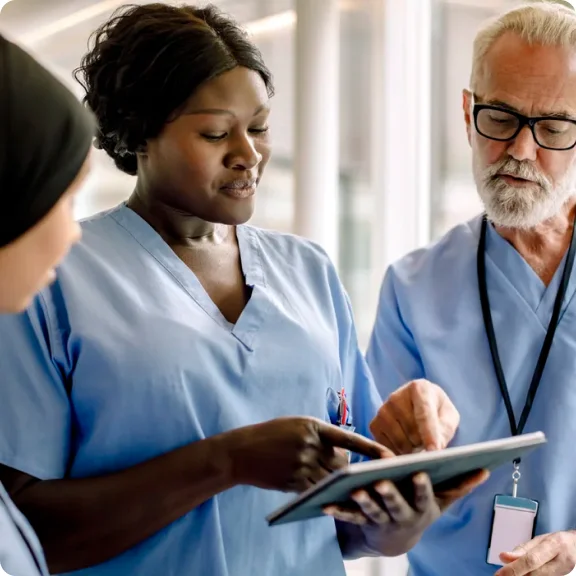 Three healthcare professionals are looking at a tablet and discussing it.